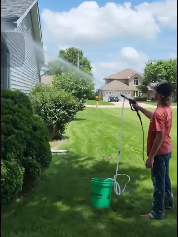 Caleb spraying water onto house siding from the front lawn