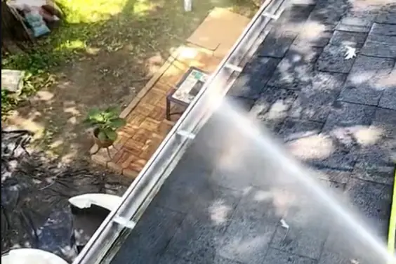 Water spraying along a white gutter on a grey shingle roof