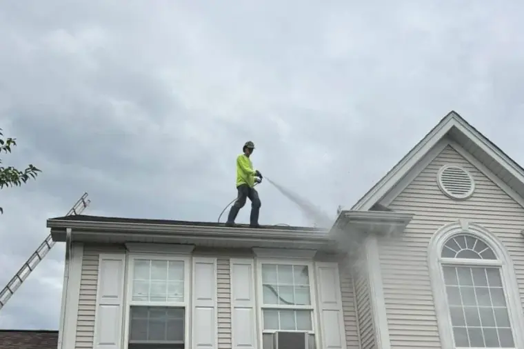 Worker in a yellow shirt spraying a grey shingle roof