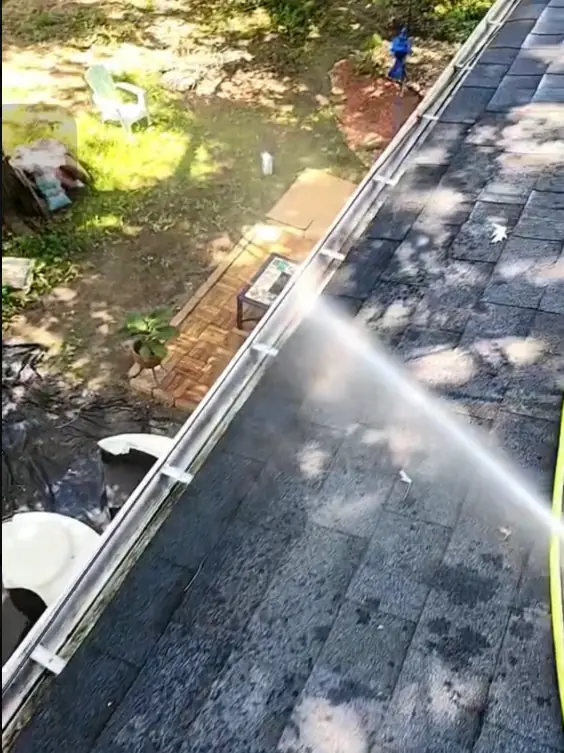 Water jet clearing leaves and grit from a white roof gutter