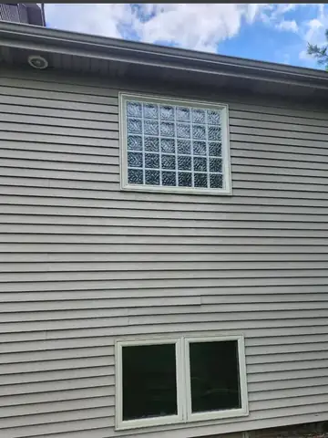 Clean grey house siding with a glass block basement window
