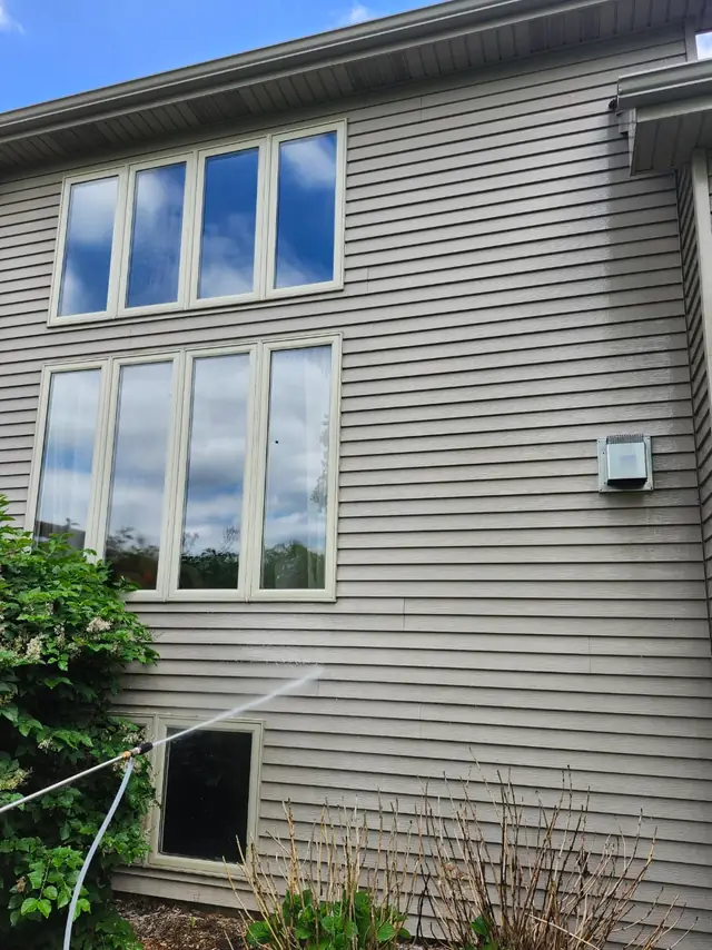 Tan house siding with tall windows being rinsed with water